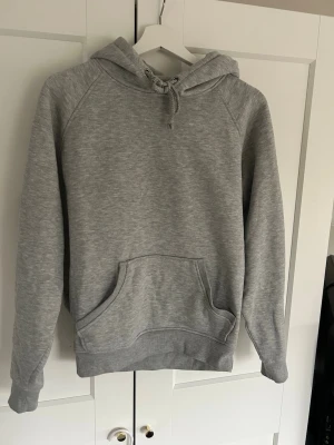 Grå basic hoodie med huva - En enkel och stilren grå hoodie med huva och dragsko, samt en ficka på magen.