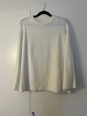 Vit oversized stickad tröja - Säljer en enkel och stilren vit stickad tröja med oversized passform. Tröjan har rund halsringning, långa ärmar och bred ribbstickad kant nedtill och vid ärmsluten. Perfekt för lager på lager och en clean look.