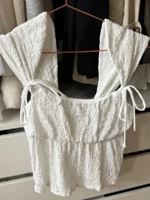 Vit linnetopp från Gina Tricot - Supersöt vit linnetopp från Gina Tricot med knytband på axlarna och en lätt rynkad struktur. Toppen är ärmlös och har en luftig, somrig känsla som passar perfekt till jeans eller kjol.