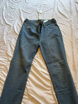 Blå Scarlett High jeans från Lee - Snygga blå jeans från Lee, modell Scarlett High med hög midja och klassisk femficksdesign. Jeansen har raka ben och är tillverkade i mjukt denimtyg med gul kontrastsöm. Perfekta för en avslappnad och trendig look.