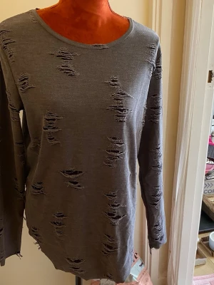 Grå distressed långärmad tröja M - Säljer en grå långärmad tröja med distressed detaljer och slitna hål över hela plagget. Tröjan har rund halsringning och är gjord i mjukt bomullsliknande material. Perfekt för en edgy och avslappnad stil.