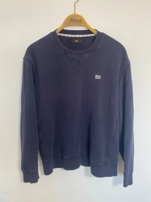Mörkblå sweatshirt från Lee - Mörkblå sweatshirt från Lee med rund halsringning och broderad logga på bröstet. Tröjan har ribbade muddar vid ärmslut och nederkant samt en klassisk relaxed passform. Perfekt för en avslappnad och stilren look. Öppet för diskussioner.