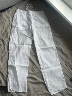 Vita linnebyxor - Säljer ett par vita linnebyxor med avslappnad passform och elastisk midja med dragsko. Byxorna är raka i modellen och tillverkade i ett lätt och luftigt linnetyg, perfekta för varma dagar. Använd ett par gånger. 