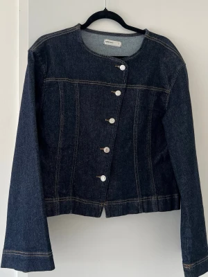 Mörkblå figursydd jeanstopp med sned knäppning - Snygg mörkblå jeanstopp/jacka med unik sned knäppning framtill och silverfärgade knappar. Toppen har rund halsringning, långa ärmar och dekorativa sömmar. Den är lite firgursydd och perfekt för dig som vill ha en stilren men ändå cool look. 🥰