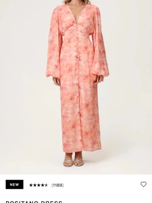 Blommig adooreklänning Positano - Långklänning i Positano-stil med blommigt mönster i rosa och ljusa toner. Klänningen har v-ringning, knappar framtill och långa, vida ärmar. Den är helt ny med lapparna kvar, aldrig använts🥰