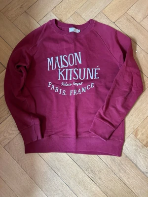Vinröd sweatshirt Maison Kitsuné - Vinröd sweatshirt från Maison Kitsuné i storlek M med vit text på bröstet. Tröjan har rund halsringning, ribbade muddar och är tillverkad i mjuk bomull. Inga defekter, nypris ~2000. Tveka inte att höra av dig vid frågor eller funderingar.😊
