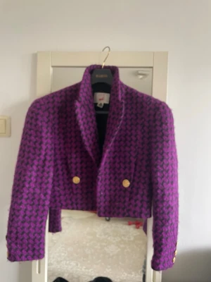 Mondi - Lila och svart cropped kavaj -  en snygg  vintage cropped kavaj från Mondi i lila och svart hundtandsmönster. Kavajen har guldknappar framtill och på ärmsluten, samt bred krage och axelvaddar och två sidor fickor. 