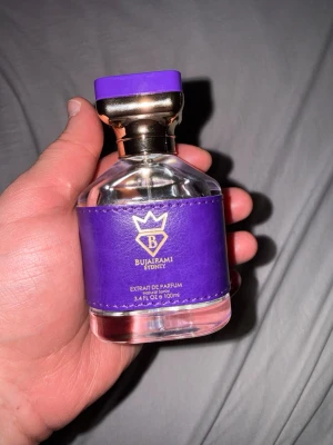 Bujarami Executor Extrait de Parfum - Lyxig parfym från Bujarami Sydney, modellen Executor. Flaskan är genomskinlig med lila och gulddetaljer samt ett lila band runt flaskan. Kommer i en snygg lila box med guldfärgad text. Innehåller 100 ml Extrait de Parfum.
