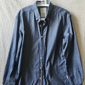 Blå skjorta från Esprit - Klassisk blå skjorta från Esprit med lång ärm och knappar framtill. Skjortan har en stilren design och är tillverkad i mjuk bomull som känns skön mot huden. Perfekt för dig som gillar en enkel men snygg look.