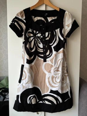 Vintage / retro klänning  - Superfin kort vintage klänning / lång topp från H&M med stora blommiga mönster i svart, beige och vit. Klänningen har knappar framtill samt fickor vid sidan! ❤️