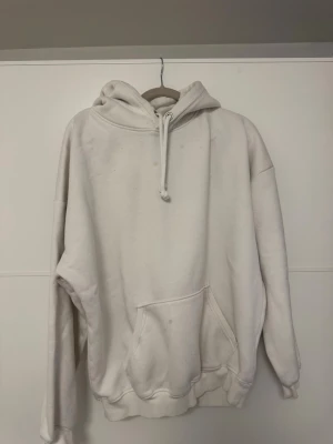 Vit oversized hoodie med ficka - Säljer en vit oversized hoodie med stor magficka och dragsko i huvan. Hoodien har en klassisk look med ribbade muddar och mjukt material, perfekt för en chill och avslappnad stil. Passar dig som gillar basic men ändå vill ha något snyggt och bekvämt. Flertalet fläckar därav billiga priset🪄