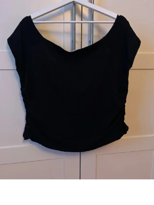 Offshoulder topp med rynkade sidor - En svart, enkel och stilren offshoulder topp med rynkdetaljer på sidorna. Toppen är ärmlös och har en lätt loose passform.  