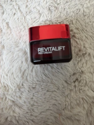 Revitalift Red Cream ansiktskräm - Revitalift Red Cream är en ansiktskräm i en snygg röd och svart burk med glansig finish. Krämen har en lätt röd ton och kommer i en fyrkantig glasburk med rött lock. Perfekt för dig som vill boosta din hudvårdsrutin. Använt några gånger. 