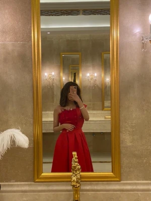 Röd axelbandslös klänning - Snygg röd axelbandslös klänning med volangdetaljer upptill och markerad midja. Kjolen är vid och faller elegant ner till ankeln. Perfekt för dig som vill sticka ut med en klassisk och feminin look.