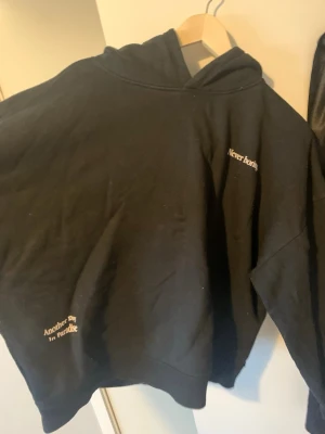 Svart hoodie med tryck - Svart hoodie med huva och vit text på bröstet och nedtill där det står 'Never boring' och 'Another day in paradise'. Oversized passform och klassisk design, perfekt för en chill och avslappnad stil.