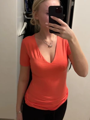 Korallfärgad v-ringad t-shirt - Säljer en snygg korallfärgad t-shirt med v-ringning och korta ärmar. T-shirten har en figurnära passform och är tillverkad i mjuk bomull, perfekt för en avslappnad och trendig look.