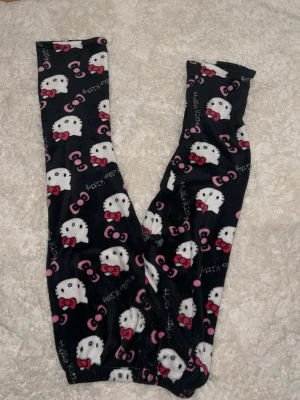 Hello Kitty mjuka loungewearbyxor - Supermysiga svarta loungewearbyxor med Hello Kitty-motiv i vitt och rosa. Byxorna är i ett mjukt, fleeceliknande material och har elastisk midja. Perfekta för chill hemma eller sleepovers med kompisar.