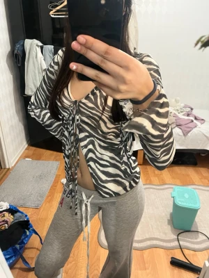 Zebramönstrad omlottopp med knyt - Trendig zebramönstrad omlottopp i svart och vitt med långa ärmar och knyt framtill. Tunn och luftig mesh-liknande polyester som ger en cool och edgy vibe. Perfekt för dig som vill sticka ut med ett djurmönster och croppad passform.