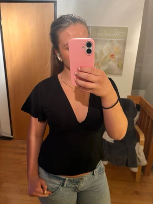 Svart topp med knytning - Svart knyttopp från GinaTricot med djup v-ringning och korta, lite fladdriga ärmar. Toppen har knytband i midjan för en snygg passform och är gjord i mjuk bomull. Perfekt till jeans eller kjol för en trendig look.💖🙌