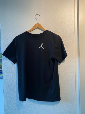Svart Jordan t-shirt  - Snygg svart t-shirt från Jordan med den klassiska Jumpman-loggan i vitt på bröstet. T-shirten har rund halsringning och korta ärmar. Perfekt för en sportig och avslappnad stil.