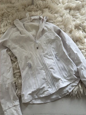 define jacket ”lululemon” - Snygg vit define jacket från ””lululemon””. Jackan har två fickor med dragkedja och är tillverkad i ett lätt material som passar perfekt för blåsiga dagar. Snygga sömdetaljer ger en sportig look. Perfekt för dig som vill ha en stilren och funktionell jacka.