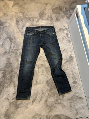 Mörkblå jeans från Lee - Snygga mörkblå jeans från Lee med klassisk femficksdesign och raka ben. Jeansen har guldfärgade sömmar och Lee-lapp bak i midjan. Tillverkade i slitstarkt denimtyg som ger en tidlös look. W33 L30
