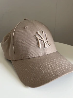 Beige New York Yankees keps - Snygg beige keps från New Era med klassisk böjd skärm och broderad NY-logga framtill. Justerbar rem baktill för perfekt passform. Tillverkad i slitstark bomull som ger en clean och stilren look. Jag säljer den för den passar inte mig