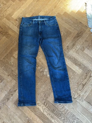 Blå raka jeans med klassisk tvätt - Säljer ett par blå jeans i rak passform från [Jack n Jones, regular Clark ].  Storlek: [W29/L30]   Skick: mycket bra / bra använt skick   Inga hål eller större defekter. Normal fading/slitage från användning.  Snygg blå tvätt som funkar till vardags.   Skriv vid frågor eller om du vill ha fler bilder/mått.