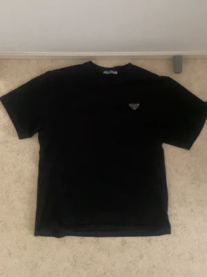  Prada t shirt accepterar alla bud - Snygg svart t-shirt från Prada med klassisk rund hals och korta ärmar. Diskret Prada-logga i metall på bröstet ger en exklusiv touch. Perfekt basplagg med stilren design och skön passform.