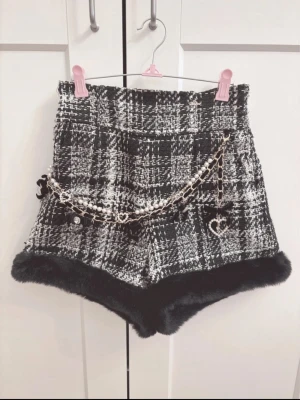 Tweed shorts liz Lisa Jirai kei ryousangata - Snygga högmidjade shorts i svartvitt rutigt tweedtyg från Liz Lisa. Shortsen har dekorativ kedja med pärlor och hjärtdetaljer samt mjuk fuskpäls vid bensluten. 