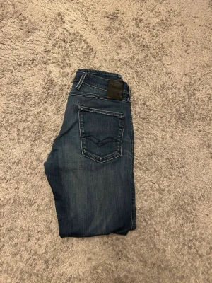 Replay anbass hyperflex - Snygga mörkblå slim fit jeans från Replay med klassisk femficksdesign och diskreta slitningar framtill. Jeansen har raka ben och detaljerade sömmar på bakfickan. Perfekta för en trendig och avslappnad look.