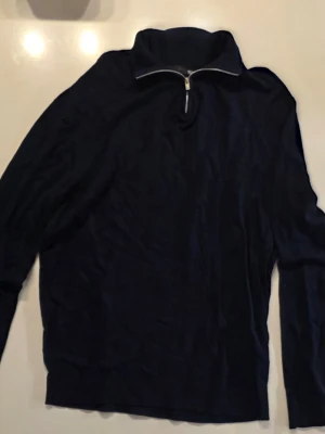 Mörkblå tröja med halv dragkedja - Mörkblå tröja med hög krage och halv dragkedja framtill. Tillverkad i mjukt stickat material och har långa ärmar. Enkel och stilren design som funkar till många olika looks         Storlek S  har på mig M vanligtvis så passar båda                                            Mått:       Bröstmått: 48 cm     Armlängd: 47 cm         Längd uppifrån:  70 cm