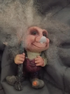 Dekorativ trollfigur med stav - Säljer en unik trollfigur med stort, lockigt grått hår och lila byxor. Figuren håller i en mörk stav och har detaljerade händer och skor, varav ena skon har en orange detalj. Perfekt som dekoration eller samlarobjekt.