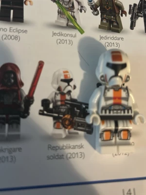 LEGO Star Wars republikansk soldat - Från 2013. LEGO Star Wars minifigur av en republikansk soldat med vit rustning, orange och svarta detaljer samt hjälm. Figurerna har tryckta detaljer på kroppen och hjälmen, och en av dem håller i ett svart vapen. Perfekt för samlare eller Star Wars-fans.