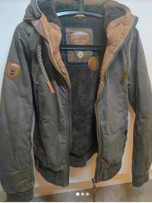 Grön vindjacka med huva Naketano - Snygg grön vindjacka med mysigt foder, huva med dragsko och ribbade muddar. Perfekt för dig som vill ha en stilren och funktionell jacka.