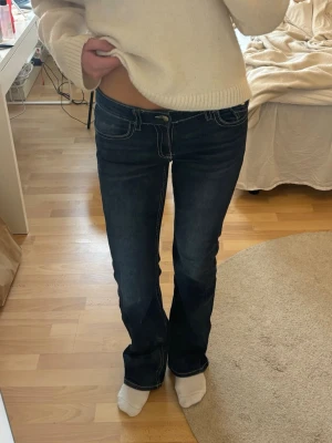 Mörkblå lågmidjade bootcut jeans  - Snygga mörkblå bootcut jeans med vita kontrastsömmar och låg midja. Säljer pågrund av att jag inte använder dom längre. Storlek 170