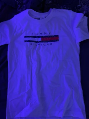 Vit Tommy Hilfiger t-shirt - Snygg vit t-shirt från Tommy Hilfiger med klassisk logga och färgblock i rött, vitt och blått på bröstet. T-shirten har rund hals och korta ärmar, perfekt till jeans eller shorts. Tillverkad i mjuk bomull för skön känsla.