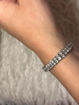 Silverfärgat armband med glittrande pärlor - Snyggt armband i silverfärg med två rader stora, glittrande pärlor som ger en lyxig känsla. Armbandet har en klassisk och stilren design som passar perfekt till dig som gillar att sticka ut lite extra. Materialet är metall med infattade pärlor.