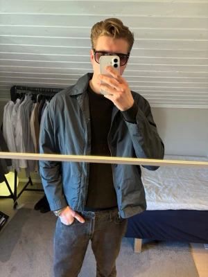 Mörkblå vindjacka från Polo Ralph Lauren - Snygg mörkblå vindjacka från Polo Ralph Lauren i klassisk modell. Jackan har dragkedja och knappar framtill, två fickor och en stilren krage. Perfekt för dig som gillar enkel och clean stil. Materialet är lätt och känns skönt att bära under vår och höst.