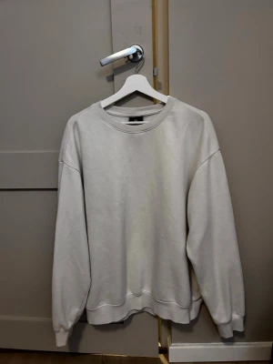 Beige sweatshirt från H&M - En basic beige sweatshirt från H&M med rund halsringning och avslappnad passform. Tröjan har långa ärmar och ribbade muddar vid ärmslut och nederkant. Perfekt för en chill och enkel stil. Tillverkad i mjukt bomullsmaterial.