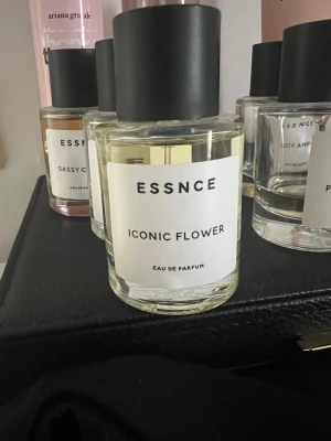 ESSNCE Iconic Flower Eau de Parfum - Fräsch parfym från ESSNCE med doften Iconic Flower. Flaskan är rund och genomskinlig med svart matt kork och enkel vit etikett med svart text. Innehållet är ljust gult. Perfekt för dig som gillar blommiga och moderna dofter. HELT NY