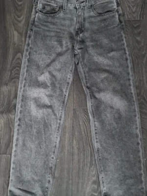 Levis 501 jeans - Säljer ett par grå tvättade jeans med rak passform och klassisk femficksdesign. Jeansen har en snygg vintagekänsla och är tillverkade i denim. Perfekta för dig som gillar en avslappnad och trendig stil.