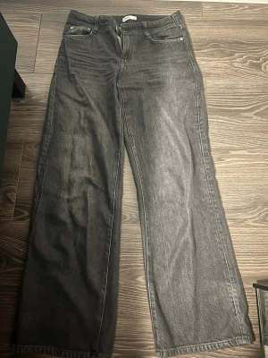 Gråa wide leg jeans från Ginatricot - Säljer ett par gråa wide leg jeans från Ginatricot i storlek 36. Jeansen har låg midja, raka och vida ben samt klassisk femficksdesign. Tillverkade i ett mjukt denimtyg som ger en avslappnad och trendig look.