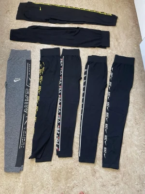 Nike och Fila mjukisbyxor med logga - Säljer flera par mjukisbyxor från Nike och Fila. Färgerna är svart och grå, med tryckta loggor längs benen i vitt, gult och rött. Byxorna har smal passform och resår i midjan. Perfekta för chill eller träning, riktigt snygga detaljer längs sidorna.