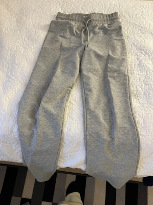 Gråa mjukisbyxor med dragsko - Säljer ett par klassiska gråa mjukisbyxor med resår i midjan och justerbar dragsko. Byxorna har en avslappnad passform och är tillverkade i mjukt sweatshirtmaterial, perfekta för chill dagar. Inga synliga loggor eller märken.