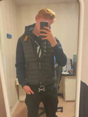 Svart dunväst från Parajumpers - Snygg svart dunväst från Parajumpers, gul detalj vid dragkedjan. Västen har två framfickor med dragkedja och quiltad design. Perfekt för en stil ren och clean look