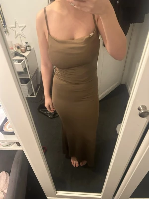 Beige långklänning med tunna band - Säljer en beige långklänning med tunna axelband och figurnära passform. Klänningen har en snygg draperad urringning och knyt i sidan för extra detalj. Perfekt för dig som gillar stilrena och eleganta plagg.