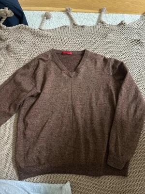 Brun V-ringad stickad tröja Sand - Mysig brun stickad tröja från Sand med V-ringning och långa ärmar. Tröjan har en enkel och stilren design med ribbade muddar vid ärmslut och nederkant. Perfekt för lager på lager och passar till det mesta i garderoben.