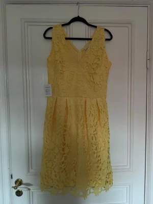 Gul spetsklänning med v-ringning - Säljer en söt gul klänning med v-ringning både fram och bak. Klänningen är ärmlös och har ett fint spetsmönster över hela tyget. Kjolen är lätt utställd och längden går till knäna. Perfekt för sommarens alla tillfällen! Oanvänd och lappen är kvar. Kommer från bonprix.