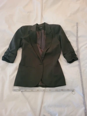 Svart kavaj med trekvartsärm från Mbym - Stilren svart kavaj från Isani med trekvartsärmar och klassisk krage. Kavajen har två fickor framtill och är helfodrad med en mjuk insida. Passformen är figurnära och materialet känns lätt och bekvämt. Perfekt för en trendig och snygg look.